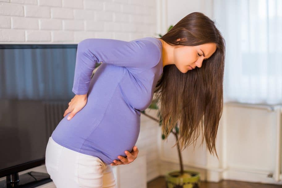 Pregnant Woman hunched over experiencing backpain.

